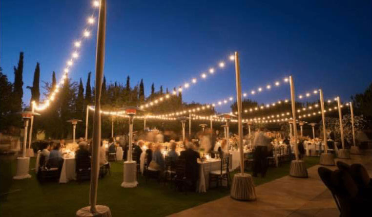 outdoor wedding reception with lights hanging above guests